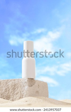 Front view of a white cosmetic bottle without label displayed on gray stone podium. Sand texture and blue sky background. Mockup scene for advertising cosmetic, space for design