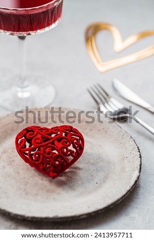 The banner. Table setting. A stylish ceramic plate, a glass of red wine, a fork and gold, red hearts on a concrete background. The concept of celebrating Valentine's Day for cafes and restaurants.