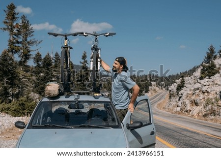 A man puts bicycles on the roof of a car on a mountain road.  Sports bikes are on the roof of the car. Traveling by car high in the mountains Royalty-Free Stock Photo #2413966151