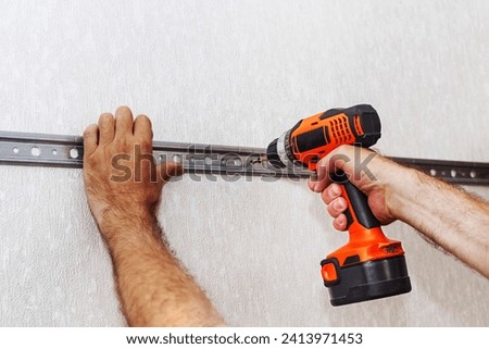 A man tightens a screw using an electric screwdriver. A carpenter. Do it yourself. Royalty-Free Stock Photo #2413971453