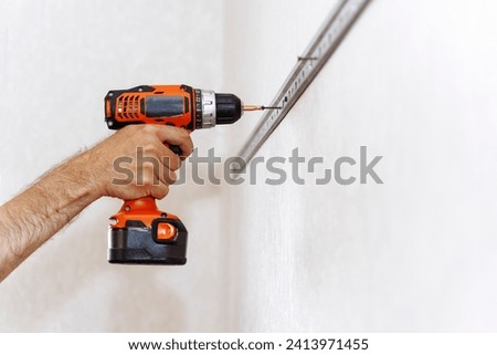 A man tightens a screw using an electric screwdriver. A carpenter. Do it yourself. Royalty-Free Stock Photo #2413971455