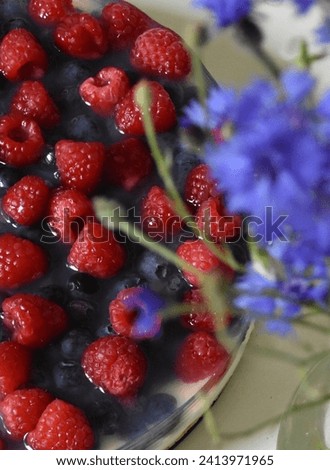 cheesecake with raspberries and blueberries and good cream and a bouquet of blue cornflowers