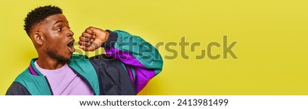 amazed trendy african american man in stylish windbreaker jacket looking away on yellow, banner