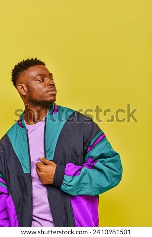 young confident african american man in bright windbreaker looking away on yellow backdrop