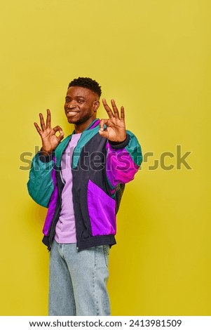 joyful african american man in stylish casual attire showing ok signs looking at camera on yellow