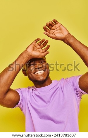 overjoyed and stylish african american man in purple t-shirt gesturing laughing on yellow backdrop