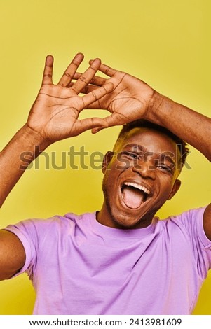 cheerful and funny african american man gesturing and sticking out tongue on yellow backdrop