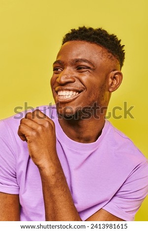 carefree african american man in purple t-shirt smiling and looking away on yellow backdrop