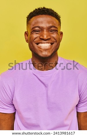 jolly african american man in purple t-shirt with radiant smile looking at camera on yellow backdrop