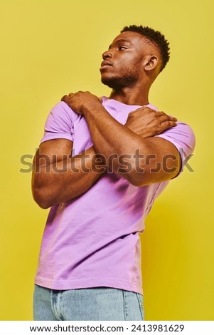 self-confident african american man in purple t-shirt posing and looking away on yellow backdrop