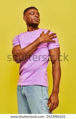 young confident african american man in  bright purple t-shirt looking away on yellow backdrop