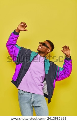 happy african american man in stylish casual attire and sunglasses dancing on yellow backdrop