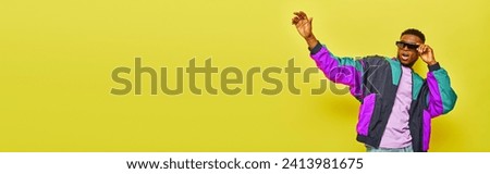 thrilled african american man in sunglasses and bright jacket waving hand on yellow backdrop, banner