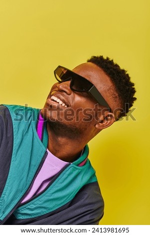 portrait of happy african american man in sunglasses and bright jacket looking away on yellow
