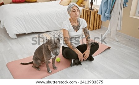 Sporty grey-haired middle-aged woman with pet dog, training yoga in serene bedroom ambiance, sitting on floor near bed for healthy workout regime