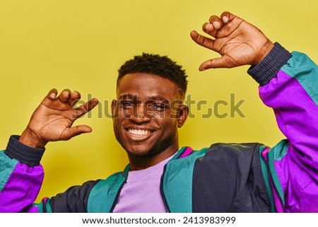 excited african american man in trendy casual clothes gesturing and looking at camera on yellow