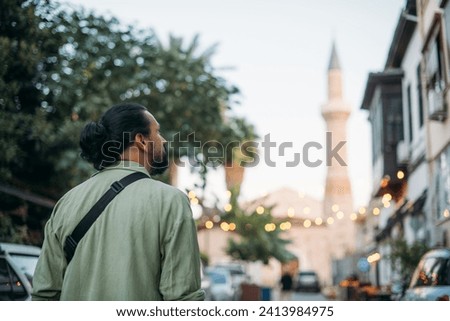 Male tourists on the picturesque street of the old Turkish city.  A young handsome guy in a shirt walks near the mosque through the narrow streets of the ancient city center Royalty-Free Stock Photo #2413984975