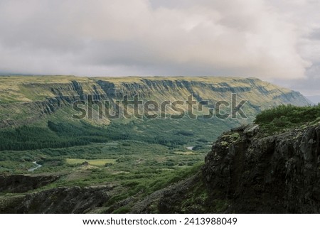 Landscape background of natural Southern Iceland countryside near Glymur waterfall with coursing rivers, evergreen trees, layered mountains, and moody cloudy sky