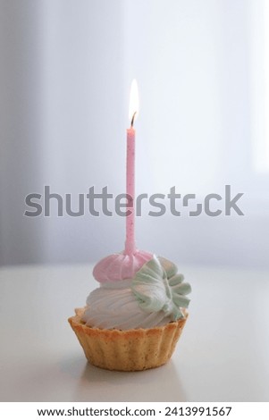 Birthday cake with burning candle on white table in light room interior, copy space for promotional text