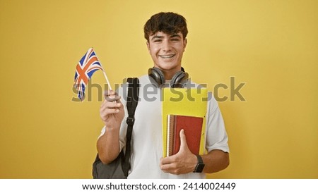 Smiling young hispanic teenager guy standing casual, smart student with books, uk flag in hand over isolated yellow background, patriotic about his english education journey Royalty-Free Stock Photo #2414002449