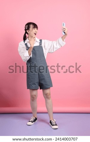 Cheerful lovely young asian woman in overalls casual clothes with gesture of taking a selfieisolated on pink background. St Valentine's Day, Women's Day, Birthday