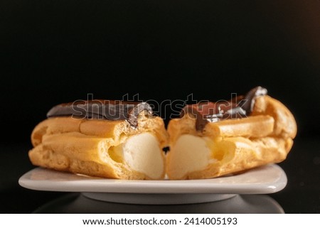 Two halves of a delicious chocolate eclair on a white ceramic plate, close-up isolated on a black background.