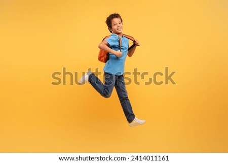 Energetic young boy with curly hair leaping joyfully, wearing blue shirt and backpack, against dynamic yellow background, capturing the essence of carefree childhood fun