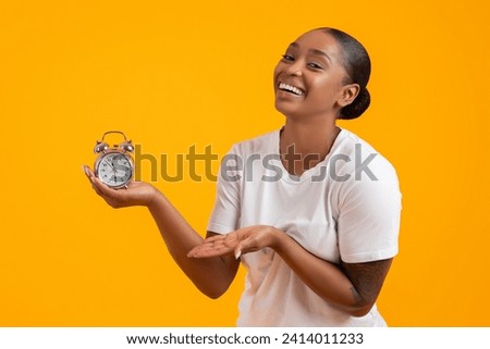 It's TIME. Happy Young African American Lady Holding Alarm Clock On Hand And Smiling, Showcasing Concept Of Deadline And Tickling Time, Posing In Casual Clothes On Yellow Studio Backdrop Royalty-Free Stock Photo #2414011233