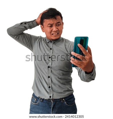 Asian man feels gloomy when looking at information on his cellphone or mobile phone, Indonesian man holds his head with a disappointed expression when looking at information on his phone. Sad man. Royalty-Free Stock Photo #2414012305