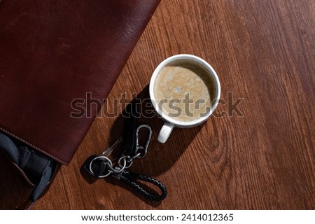 top shot of a cup of hot coffee, bike Keys and bag on a wooden textured table in cafe. Dark theme picture.