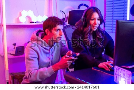 Couple or friends have shocking, exciting face with fun, using joystick to compete and play games together, sitting in room at home with neon decorated light. Game online streamer Concept