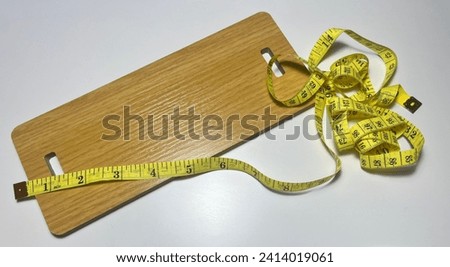 Wooden cutting board with a measuring tape on a white background.