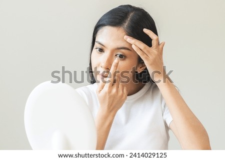 Ophthalmology care, eye sight, vision concept. Asian young woman, female hand holding and putting, wearing soft contact lenses with finger on face, girl looking in mirror at home. Medicine and health. Royalty-Free Stock Photo #2414029125