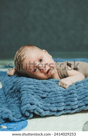 Photo of a baby in a knitted overall. A small newborn boy lies on a gray knitted blanket. Portrait of a one-month-old baby