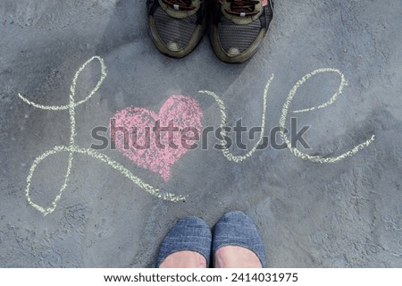 A male and female couple standing next to the word LOVE written in sidewalk chalk, feet shoes