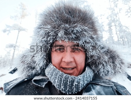close-up portrait of a smiling Caucasian middle-aged man in a winter fur hat in the forest and with frost on his face from the frost. Winter walk in the forest