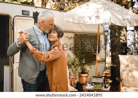 Old senior happy couple spouses dancing, spending romantic date together while on holiday in camper van, caravanning by trailer motor home Royalty-Free Stock Photo #2414041895