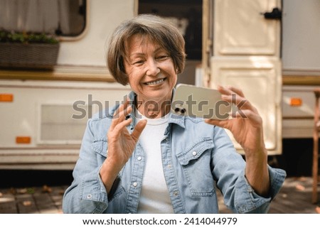 Happy smiling caucasian senior old elderly woman businessman grandmother having online conversation on cellphone vlogging blogging remotely while traveling by camper van trailer motor home