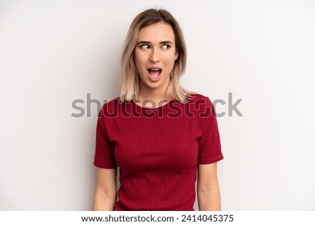 young adult blonde woman feeling shocked, happy, amazed and surprised, looking to the side with open mouth
