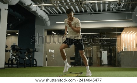 Caucasian sportsman man footballer soccer player training in sports gym exercise with ladder sport equipment workout cardio exercising jumping prepare for football match male athlete in fitness club Royalty-Free Stock Photo #2414045477