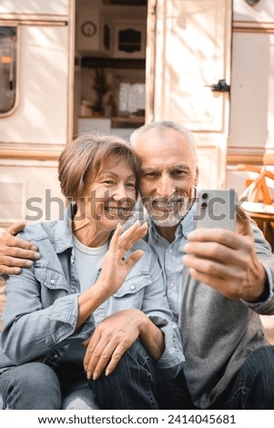 Vertical shot of senior old elderly caucasian mature couple grandparents having videocall conversation online on cellphone while traveling by trailer motor home camper van