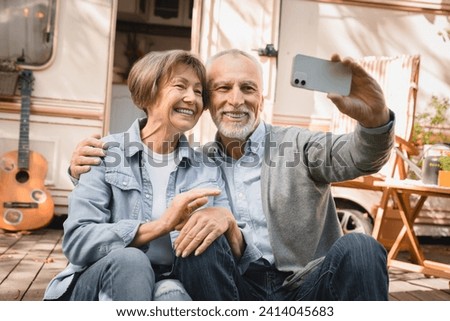 Senior old elderly caucasian mature couple grandparents having videocall conversation online on cellphone while traveling by trailer motor home camper van