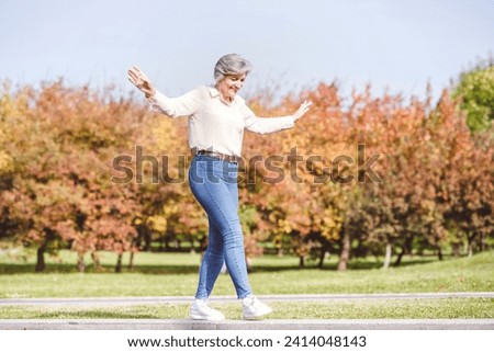 Smiling woman with arms outstretched walking on edge of street road at city