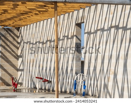Shadow pattern of roof trusses along interior of two concrete walls of a single-family house under construction in a suburban residential development on a sunny August morning in southwest Florida
