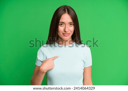 hispanic pretty woman looking proud, confident and happy, smiling and pointing to self or making number one sign