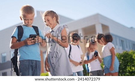 children lifestyle group school children look at smartphone video. school learning kid concept. group of kids with backpacks playing smartphone near the school building outdoors