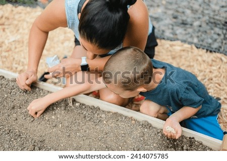 High angle of mom and young kid planting seeds in garden together Royalty-Free Stock Photo #2414075785