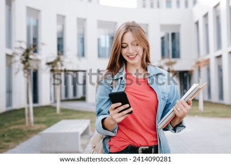 Smiling young blond female student using smart phone at university
