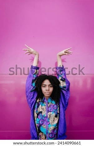 Young woman with raised arms and graceful hands in front of pink wall Royalty-Free Stock Photo #2414090661