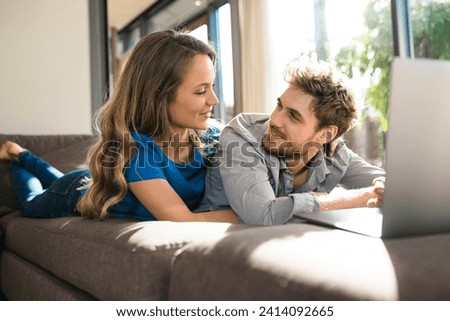 Smiling couple with laptop lying on sofa at home Royalty-Free Stock Photo #2414092665